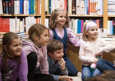 Gruppe lachender Kinder hört gespannt bei einer Lesung zu